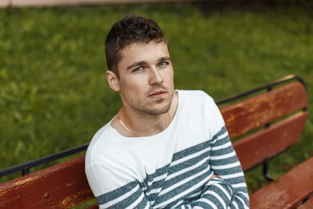 Man in a stylish pullover sitting on a bench.
