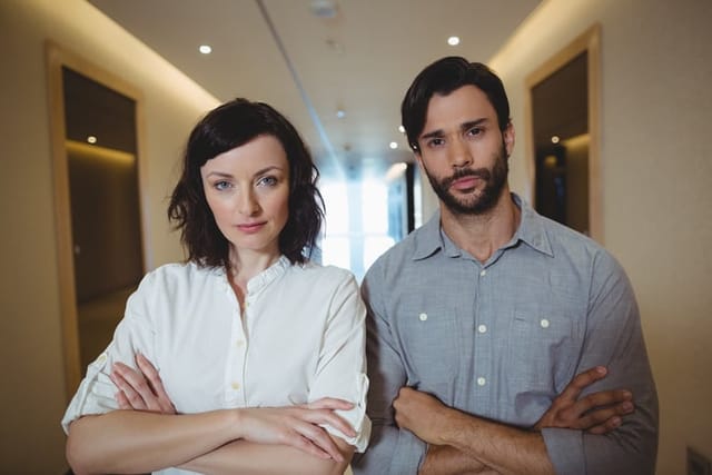 Portrait of male and female business executives standing with arms crossed in corridor at office
