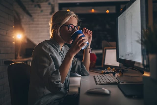 woman drinking coffee while working at computer at night
