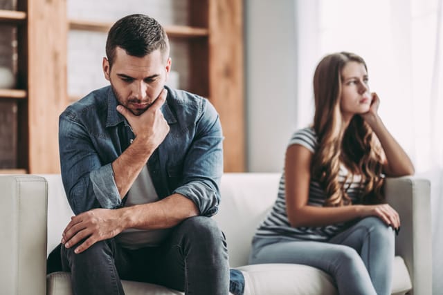 Upset couple at home. Handsome man and beautiful young woman are having quarrel. Sitting on sofa together. Family problems.