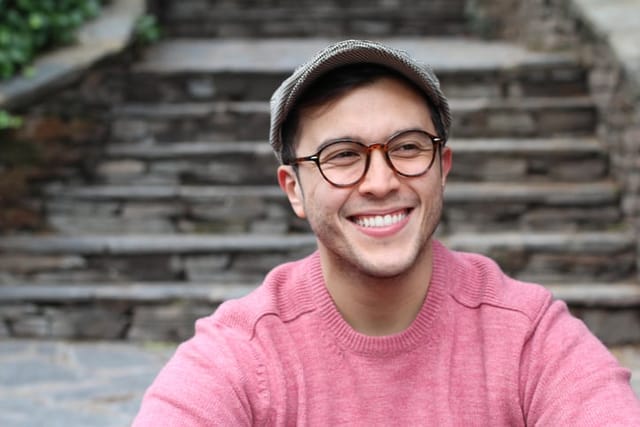 smiling man with glasses, pink shirt sitting on stairs