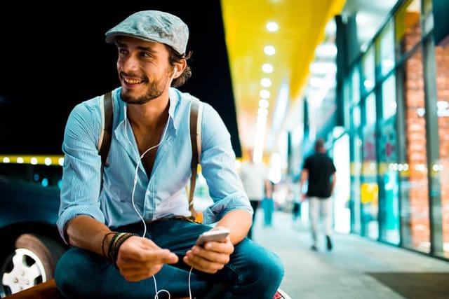 Hipster playing music or podcast on phone, listening with earbuds