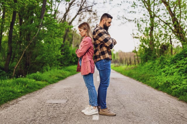 couple standing back to back in forest road