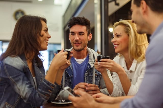Candid shot of small group of friends sitting together at the table in a coffee shop, chatting and enjoying coffee.