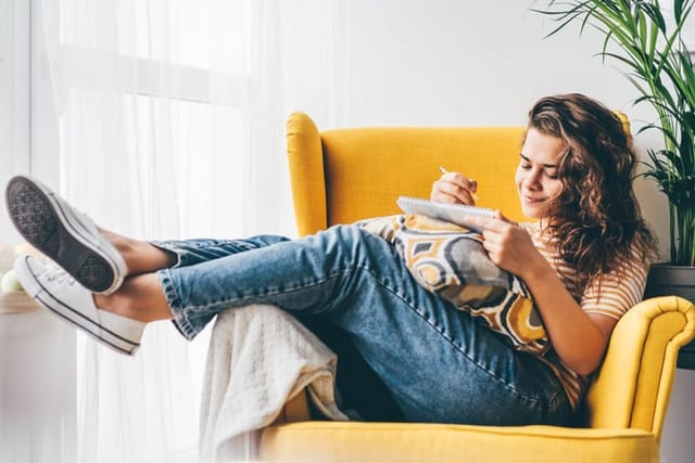 woman writing in notebook on chair