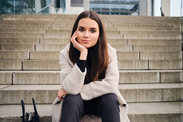 Beautiful smiling brunette girl dreamily looking in camera resting on stairs outdoor