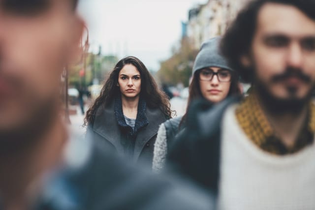 Portrait of a serious young woman among other defocused faces on the street