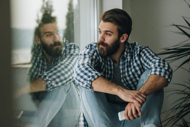 Thoughtful man relaxing on window sill at home.