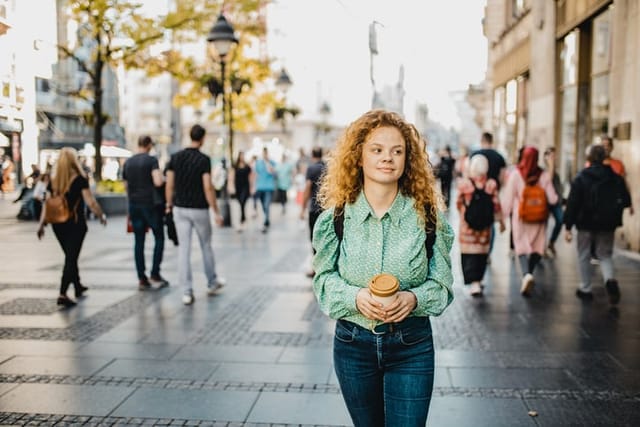 A young girl is walking down the street, there are passersby behind her, she feels lonely