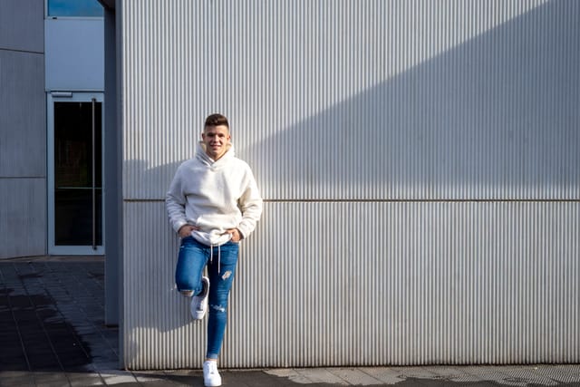 young guy in jeans and hoodie standing by wall