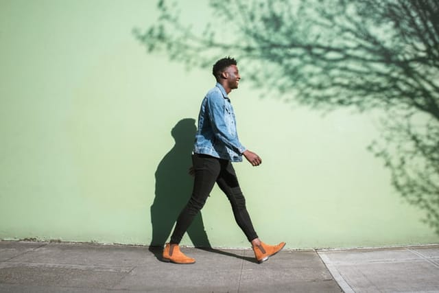 A young adult African American enjoys the sunshine as he strolls down a city walkway. The bright sunlight casts interesting shadows on the wall behind.