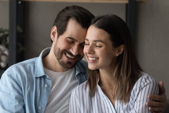 Couple in love embracing sit together on sofa. Loving handsome husband touch foreheads with beloved wife, feeling bond enjoy tender moment. Romantic relations, care, happy marriage, harmony concept