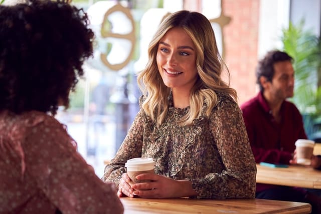 Female Friends Meeting And Talking At Table In Coffee Shop.
