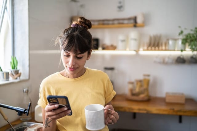 Young woman looking at her phone and drinking coffee