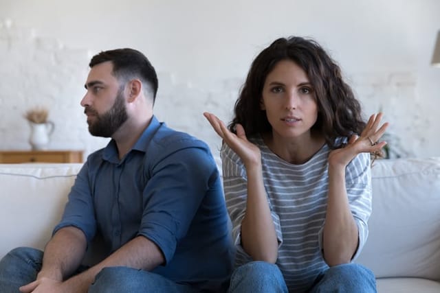 Annoyed married couple sitting on couch apart after conflict.