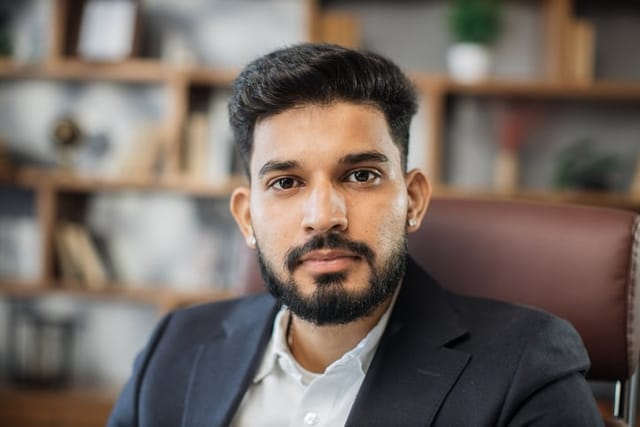 Close up portrait of bearded handsome successful middle east smiling businessman sitting at chair, working in his modern office.
