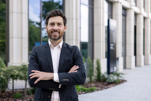 Portrait of a handsome young businessman, manager, leader standing in a suit near the office center and crossing his arms confidently smiling at the camera.