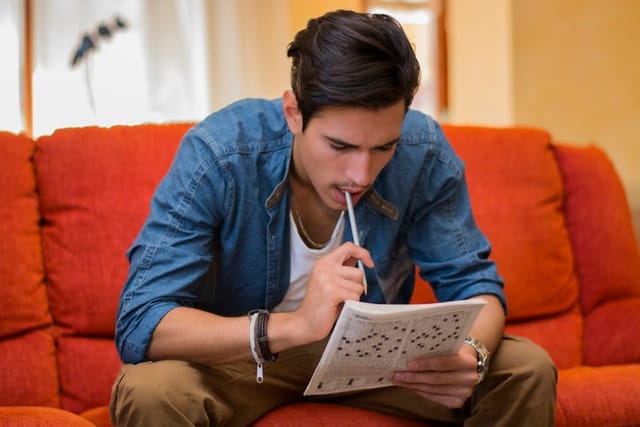 Young man sitting doing a crossword puzzle.
