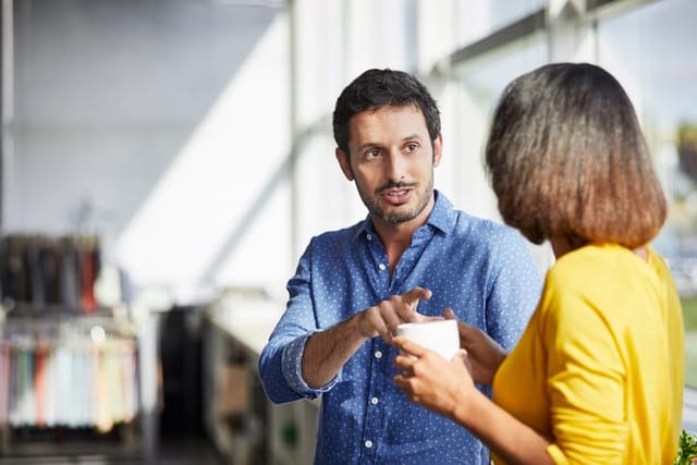 Confident businessman communicating with colleague having coffee. Male and female professionals are standing in office. They are discussing strategies at textile industry.