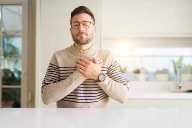 Young man smiling with hands on chest and grateful gesture on face.