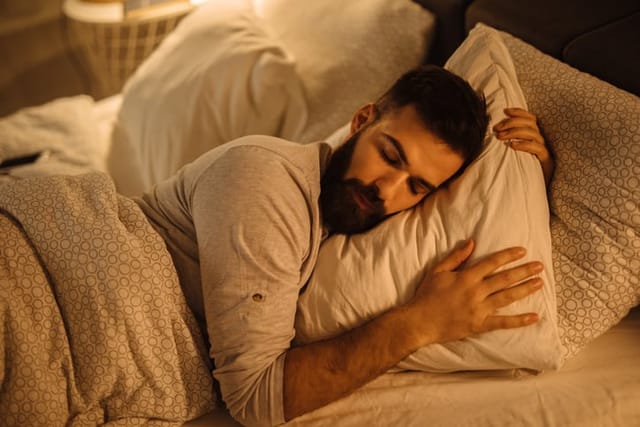 Young man sleeping in bed hugging a soft white pillow.