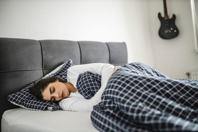 Young woman lying down on her bed in pain.