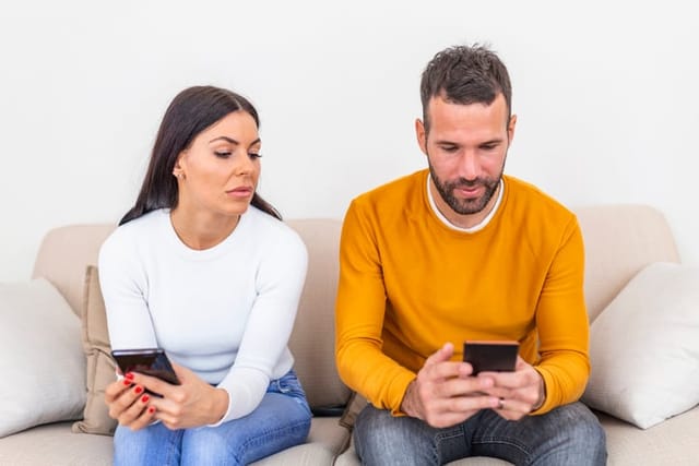 Jealous young woman with smartphone looking at boyfriend.