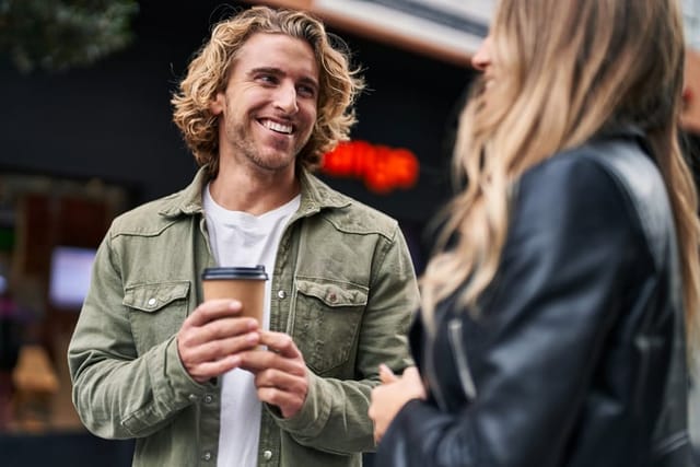 Man and woman smiling and drinking coffee on the street.