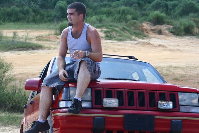 Man sitting on his car waiting for someone.