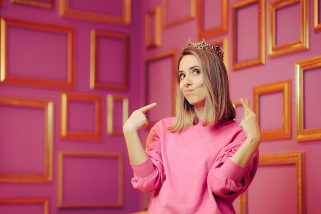 Woman wearing a crown pointing to herself.