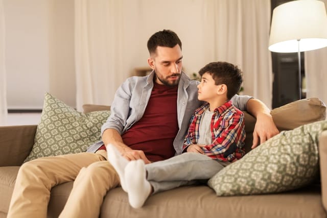 A father and his young son sitting on the couch with their arms around each other
