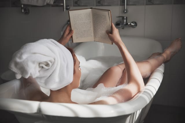 Woman in the tub reading a book.