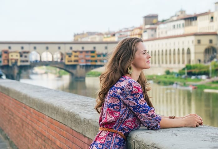 Remarkable holiday in Florence. Portrait of pensive young woman in a dress on the embankment near Ponte Vecchio