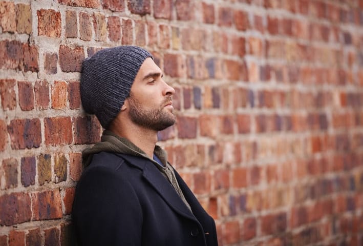 Cropped shot of a fashionable man leaning against a brick wall in an urban setting