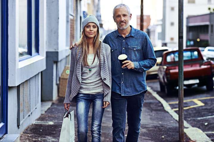 A beautiful young woman and her father walking with a shopping bag and takeaway coffee in the city
