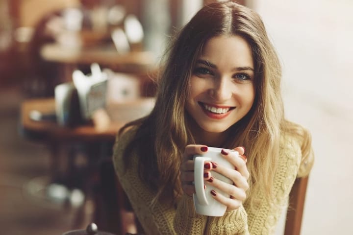 smiling woman cradling tea cup at cafe