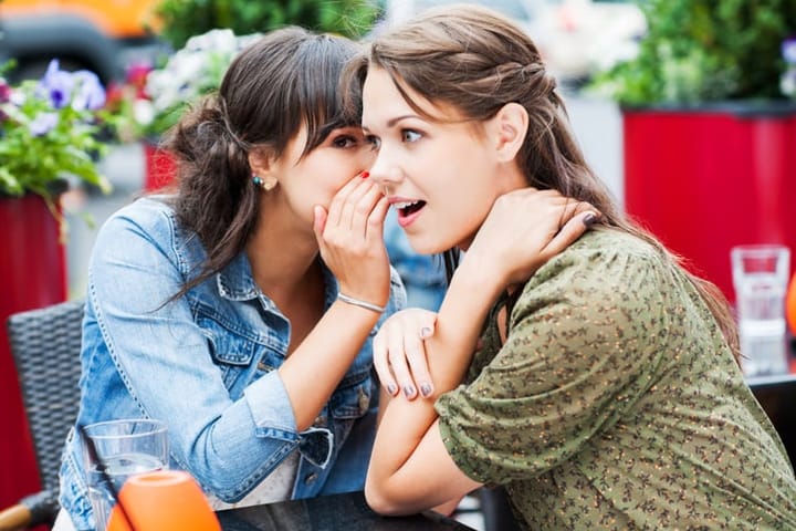 Two female friends sitting in a sidewalk cafe. They are whispering and gossiping.