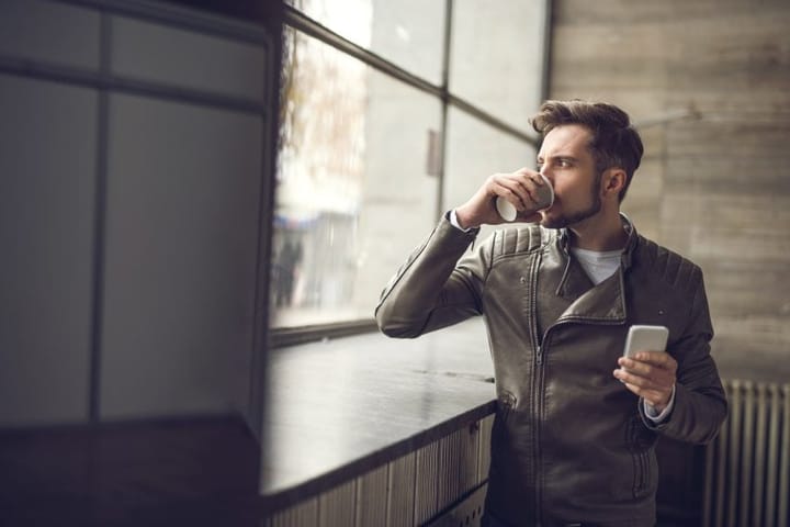 Young man drinking coffee and looking through window.
