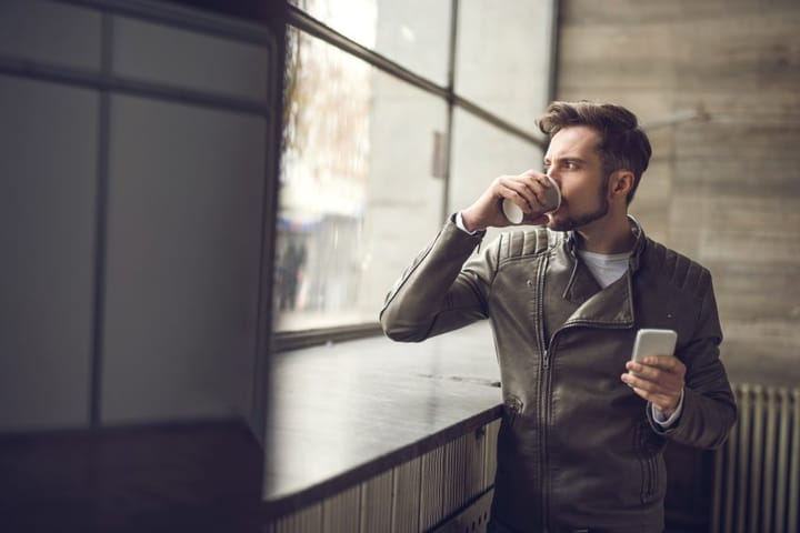 Young man drinking coffee and looking through window.