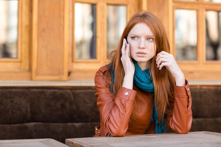 Worried concerned woman talking on cellphone in outdoor cafe