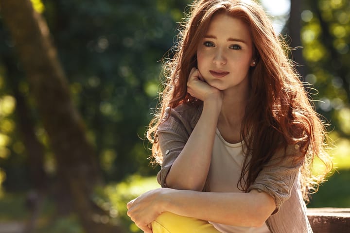 Portrait of beautiful red hair woman.She sitting at the park on beautiful summer day.