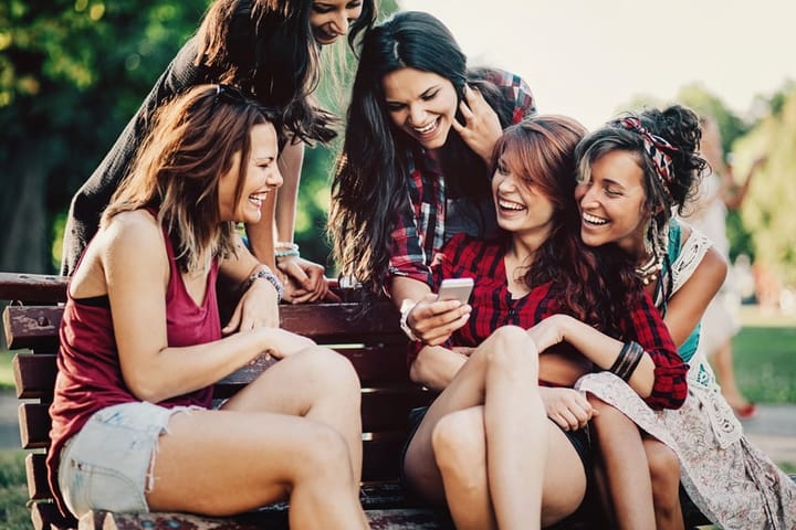 Teenage girls smiling in the park and using smart phone
