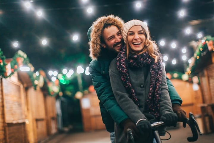 Romantic couple is riding a bike together among bungalows on the Christmas market