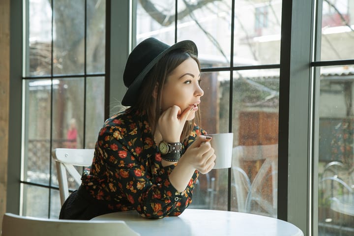beautiful woman in hat drinking coffee in the morning sitting by the window. view from inside.