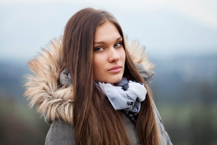 Close-up portrait of attractive young woman in front of blurry background. She is wearing a grey jacket and looking into the camera. Autumn atmosphere, selective focus.