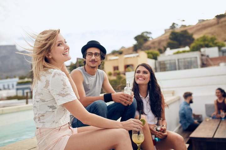 Group of young people sitting outdoors having drinks. Multiracial young friends enjoying during a rooftop party.