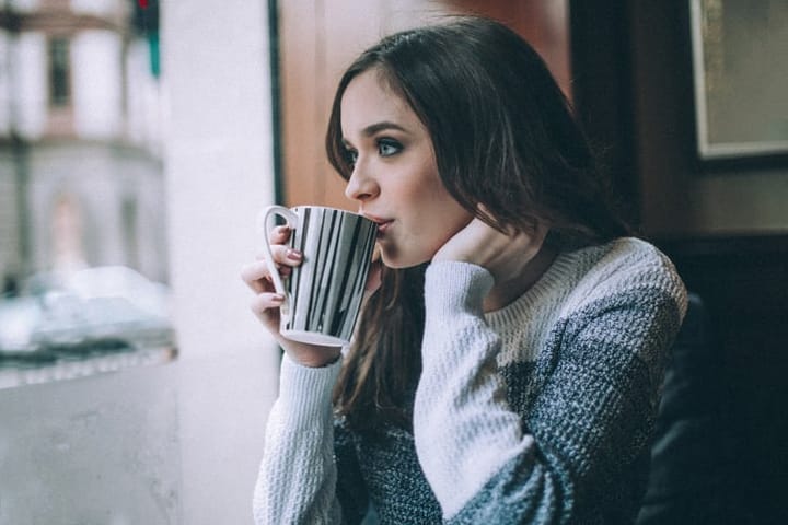 Young beautiful woman sitting in a caffe, looking through the window while drinking coffee on a rainy day.