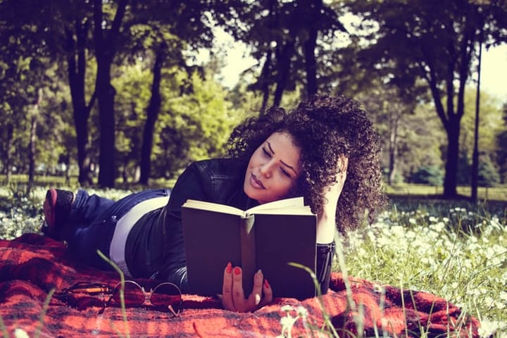 young woman read a book in park on blanket on sunny day