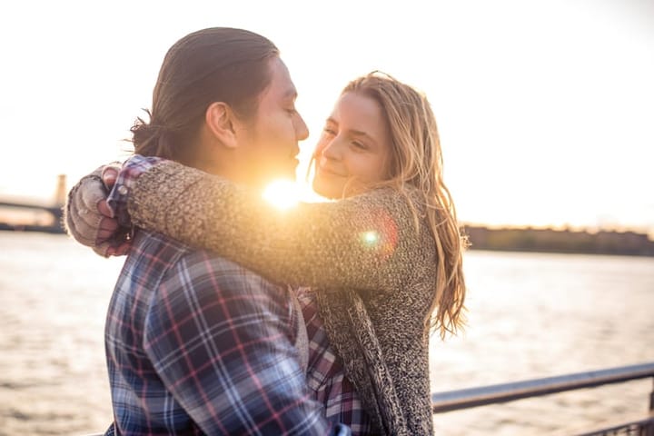 oung couple is standing on a pier. They are looking at each other and hugging. New York in the back.