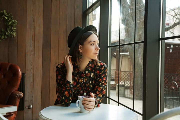 beautiful woman in hat drinking coffee in the morning sitting by the window. view from inside.